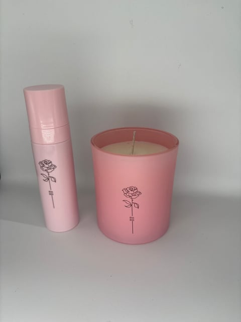 Pink cylindrical candle and matching spray bottle with rose stem design on light background