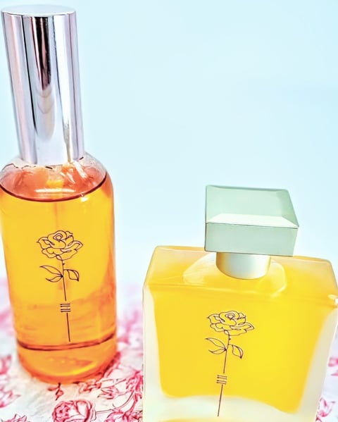 Two yellow perfume bottles with rose designs on a floral patterned surface against a light blue background