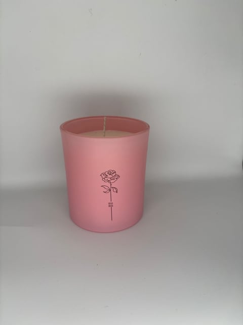 Pink cylindrical candle with a simple rose illustration printed on the front, displayed against a white background